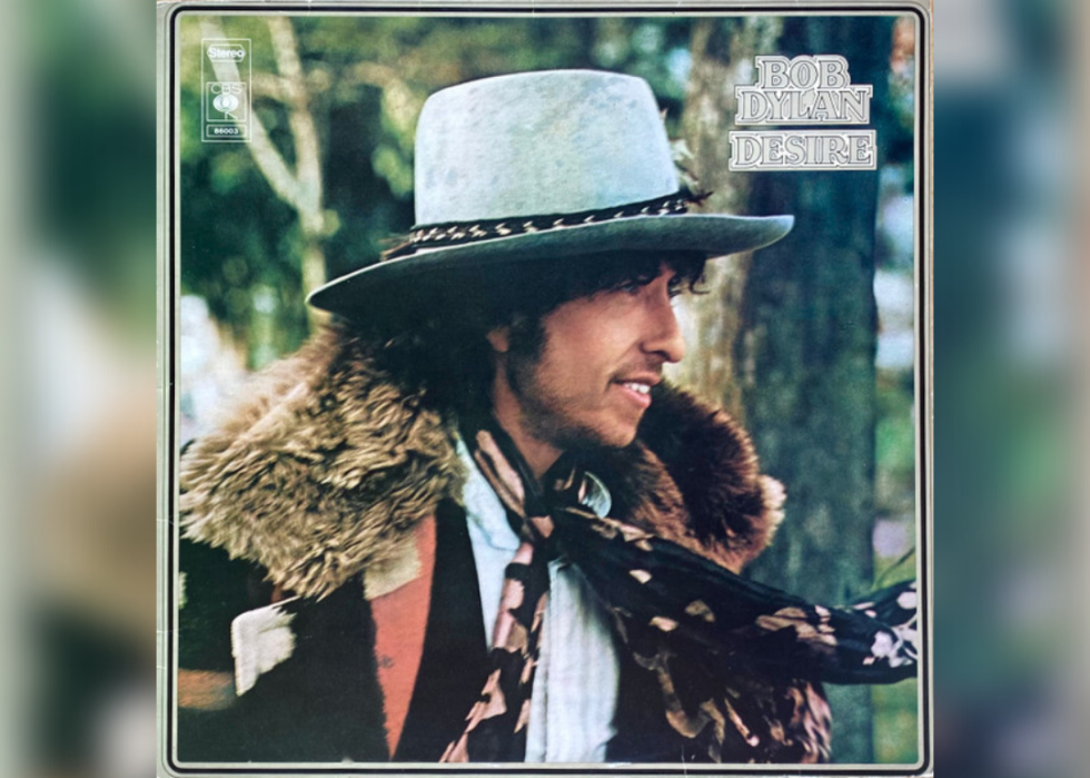 Bob Dylan looking away smiling wearing a cowboy hat, scarf and fur collared coat.