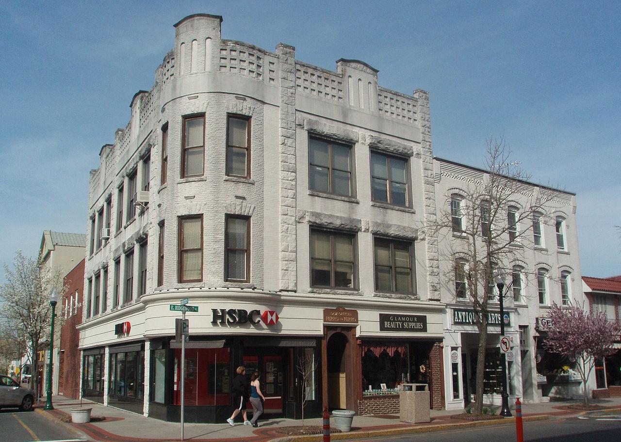 A historic gray stone corner building on a street lined with businesses.