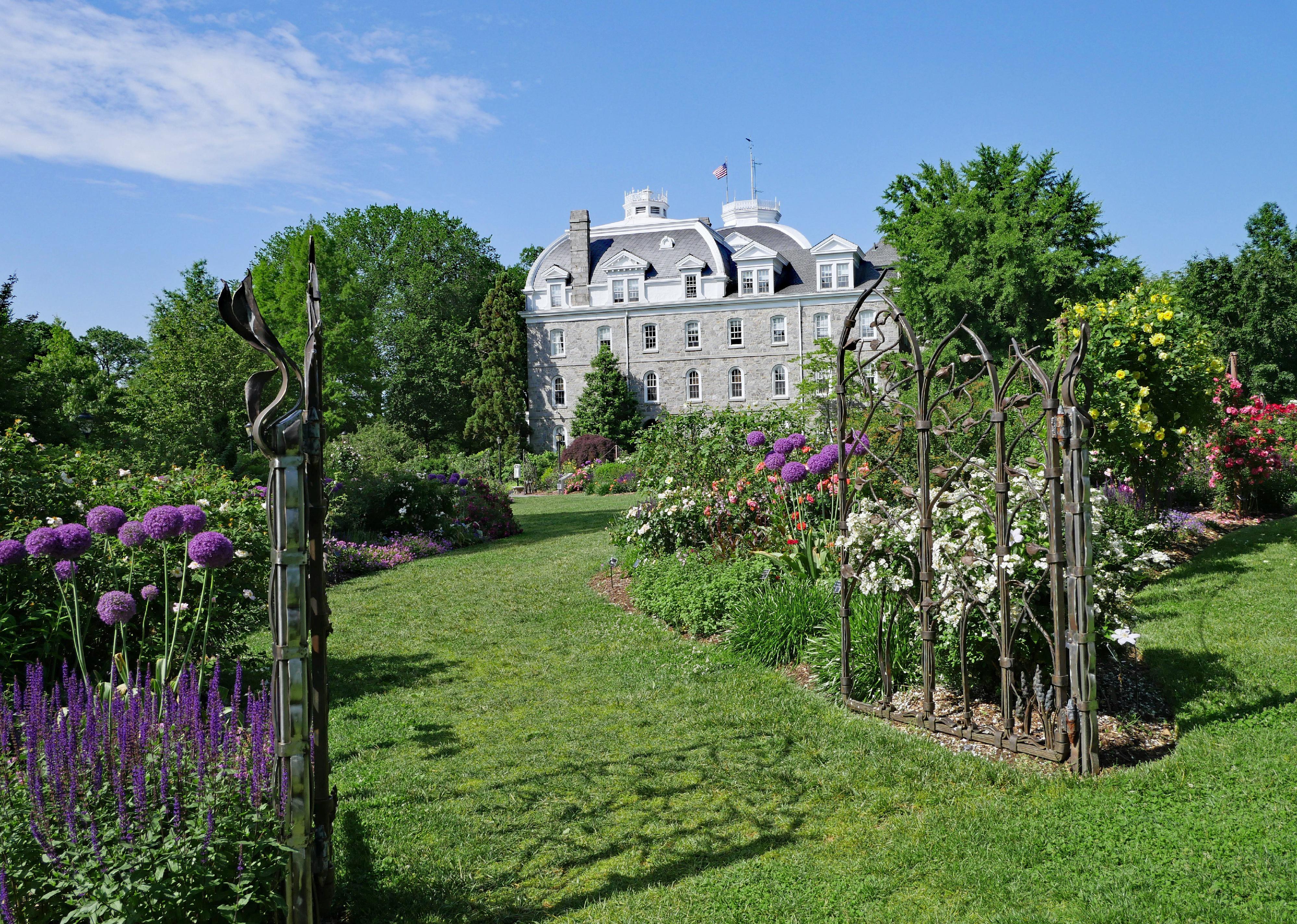 A large historic gray stone home surrounded by blooming gardens.