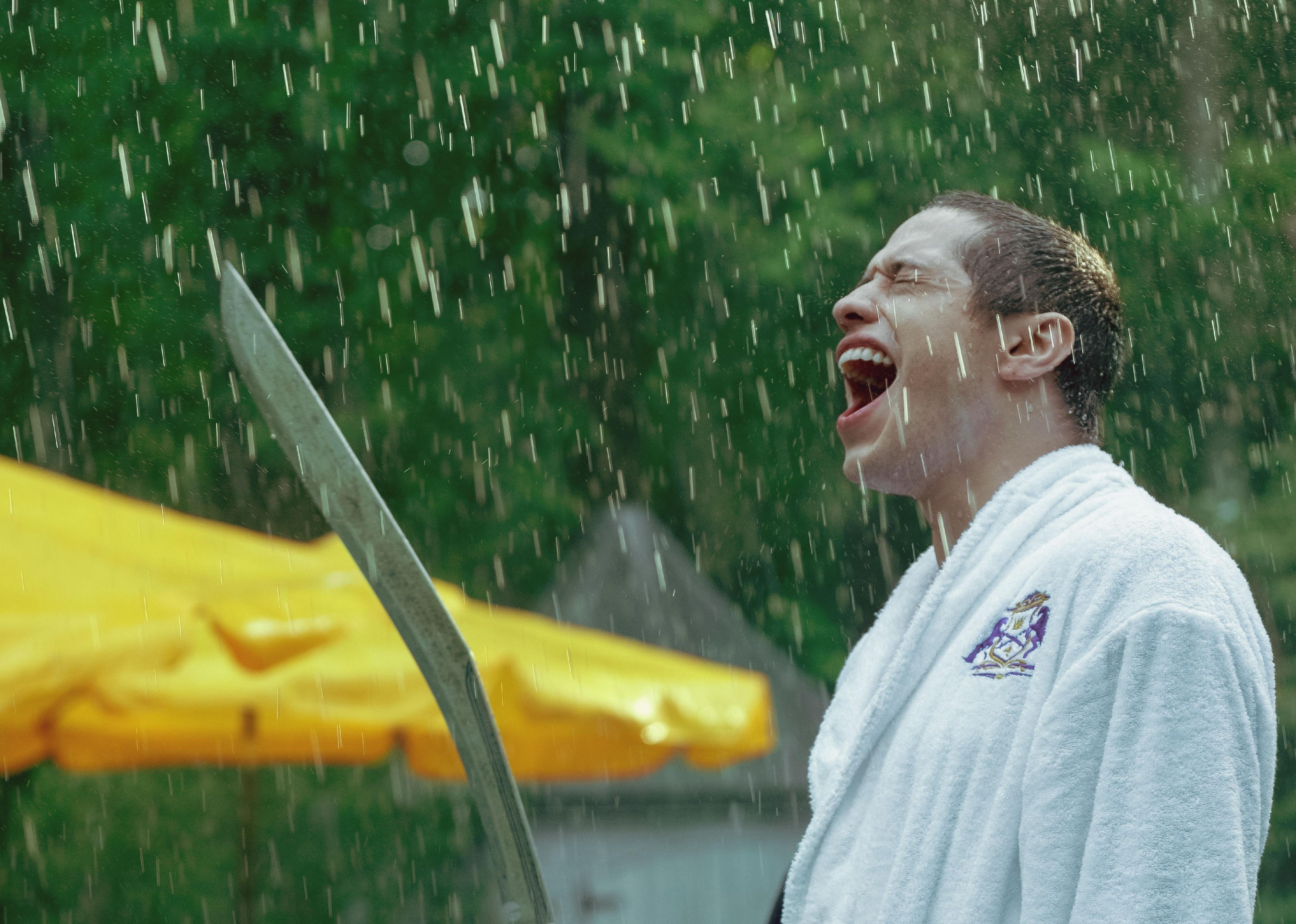 Pete Davidson wearing a robe in the rain while screaming and holding a saber