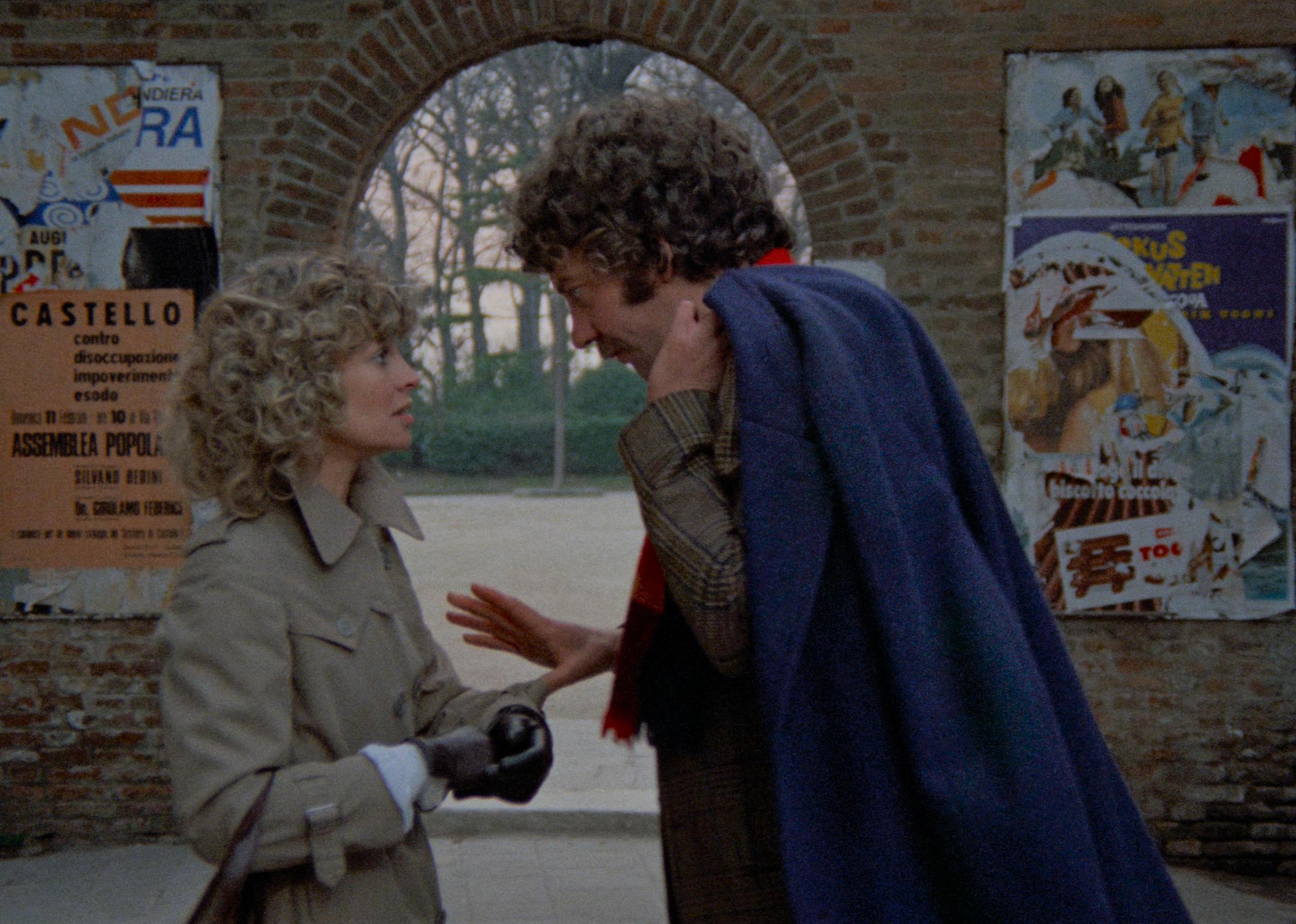 Julie Christie and Donald Sutherland talking in front of a brick archway.