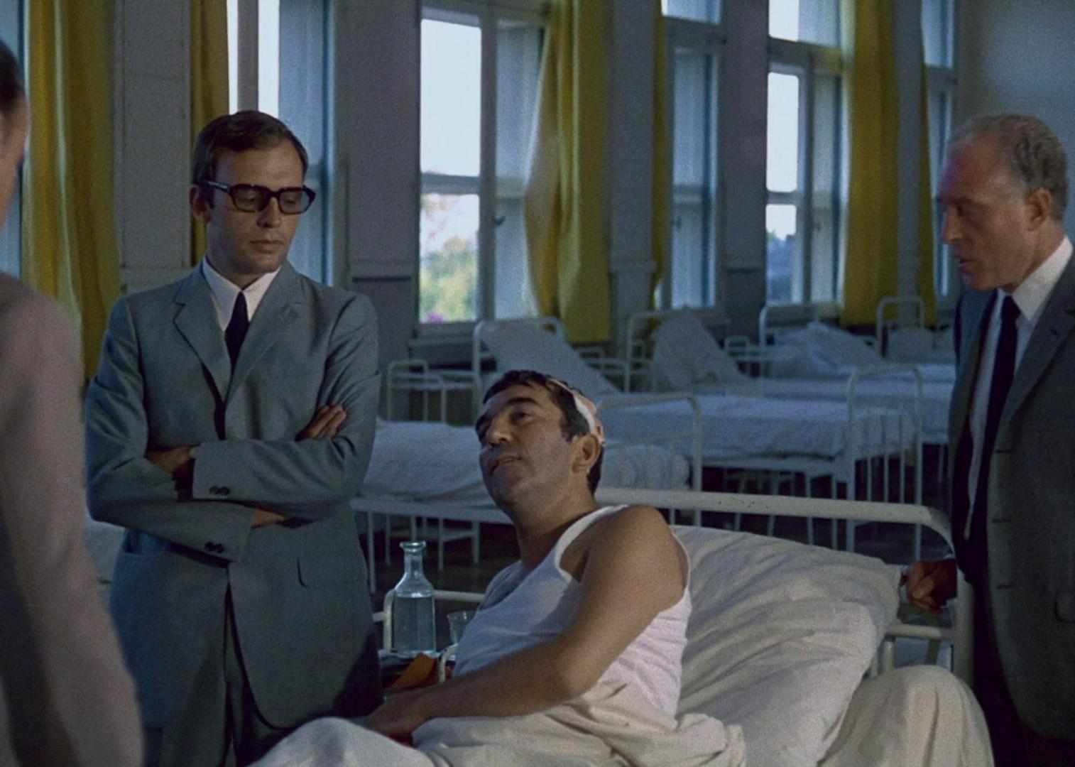 A man on a hospital bed surrounded by men in suits.