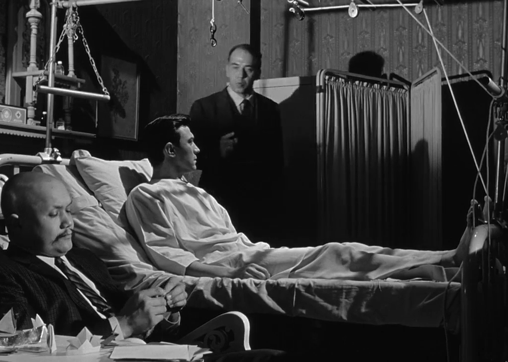 A man in a hospital room surrounded by men in suits.