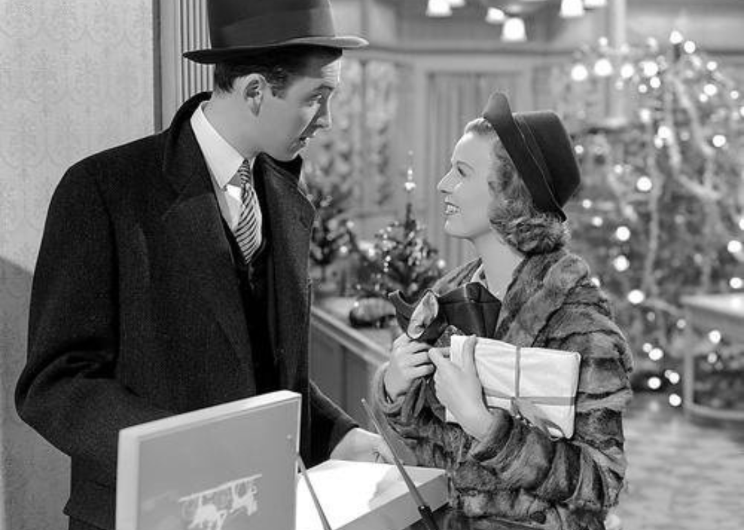 James Stewart stands smiling at a woman in a Christmas shop.