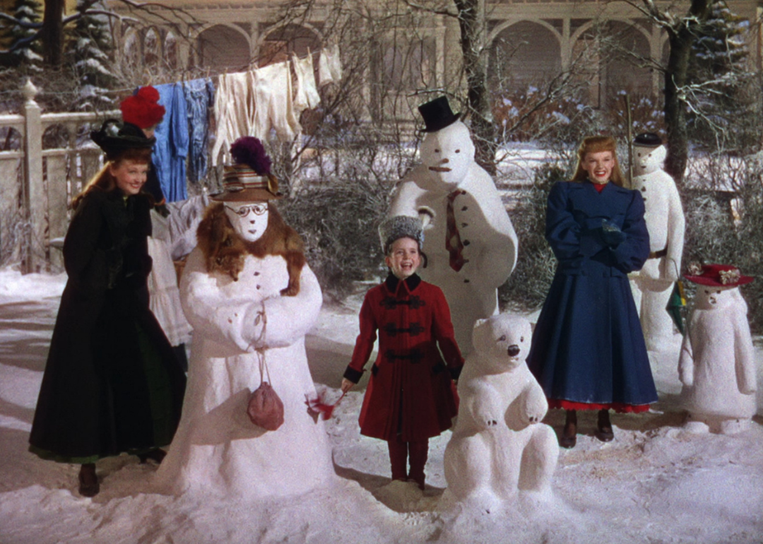 Judy Garland laughing with a woman and little girl in the middle of snowmen and bears made of snow.