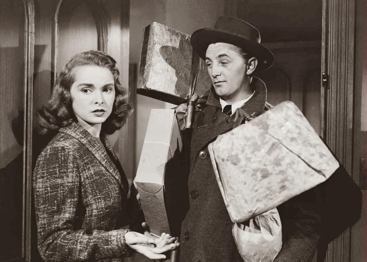 A woman opens the door to a man holding wrapped gifts.