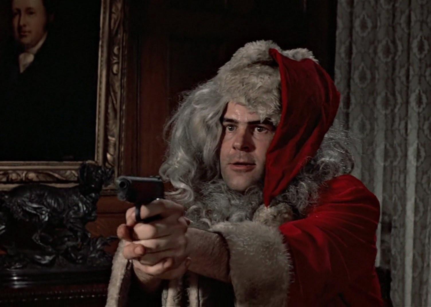 Dan Aykroyd in a santa suit pointing a gun.
