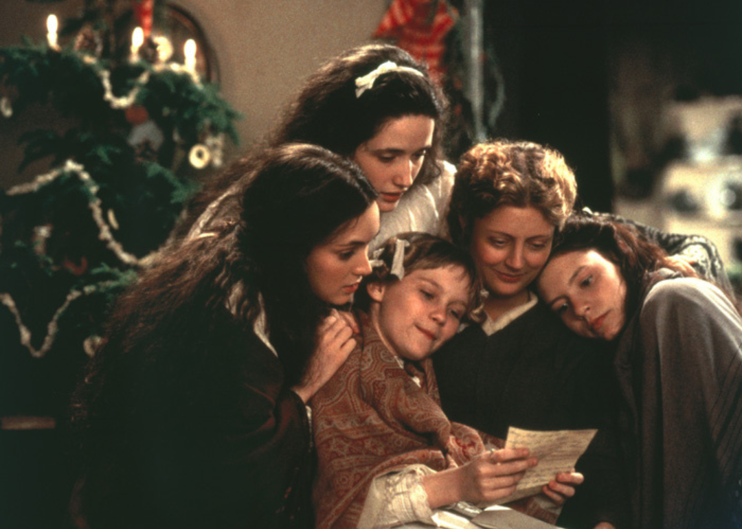 Claire Danes, Winona Ryder, Susan Sarandon, Kirsten Dunst, and Trini Alvarado crowded with arms around one another reading from a piece of paper in front of the Christmas tree.
