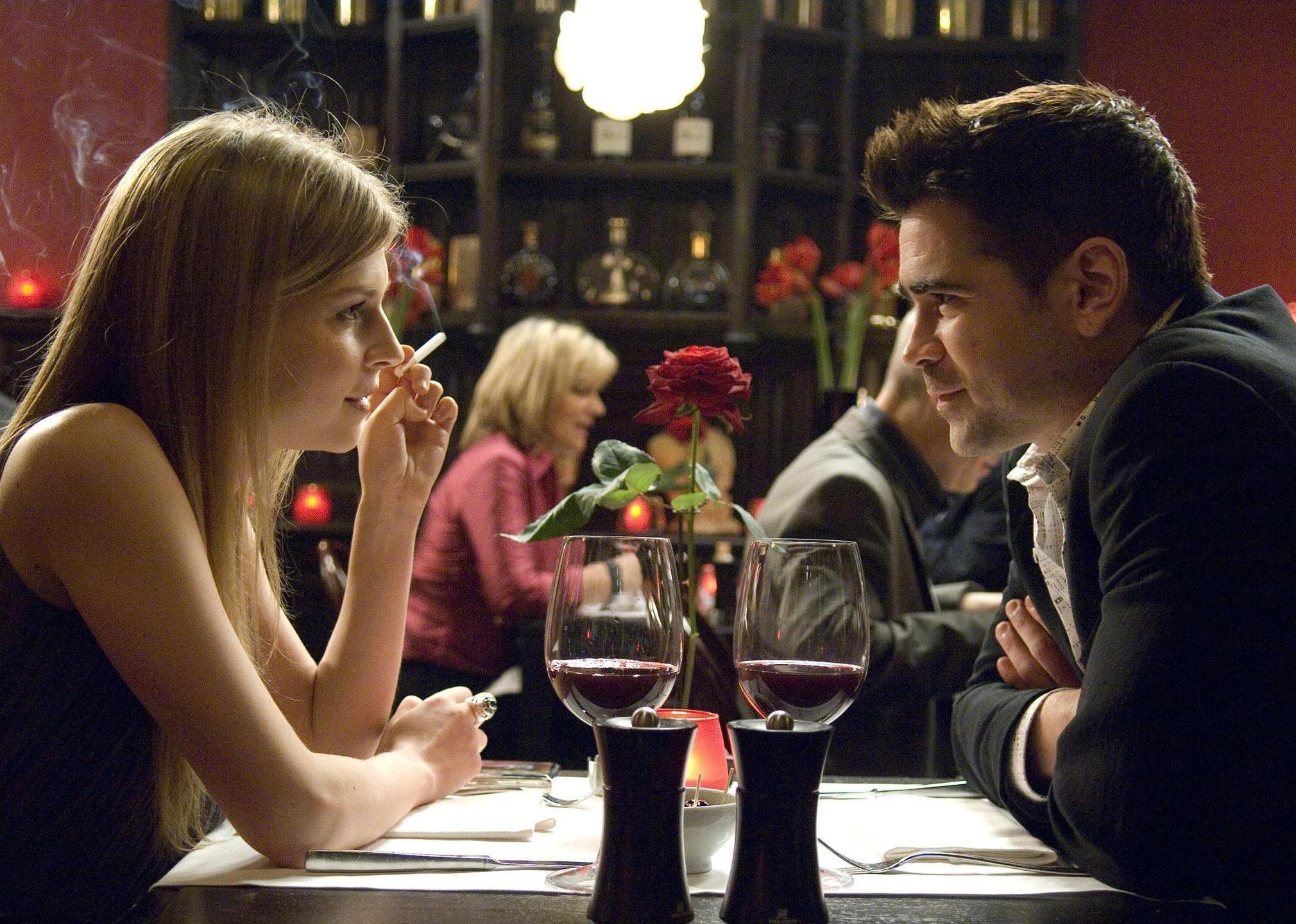 Colin Farrell sitting at a restaurant table with a woman smoking a cigarette.