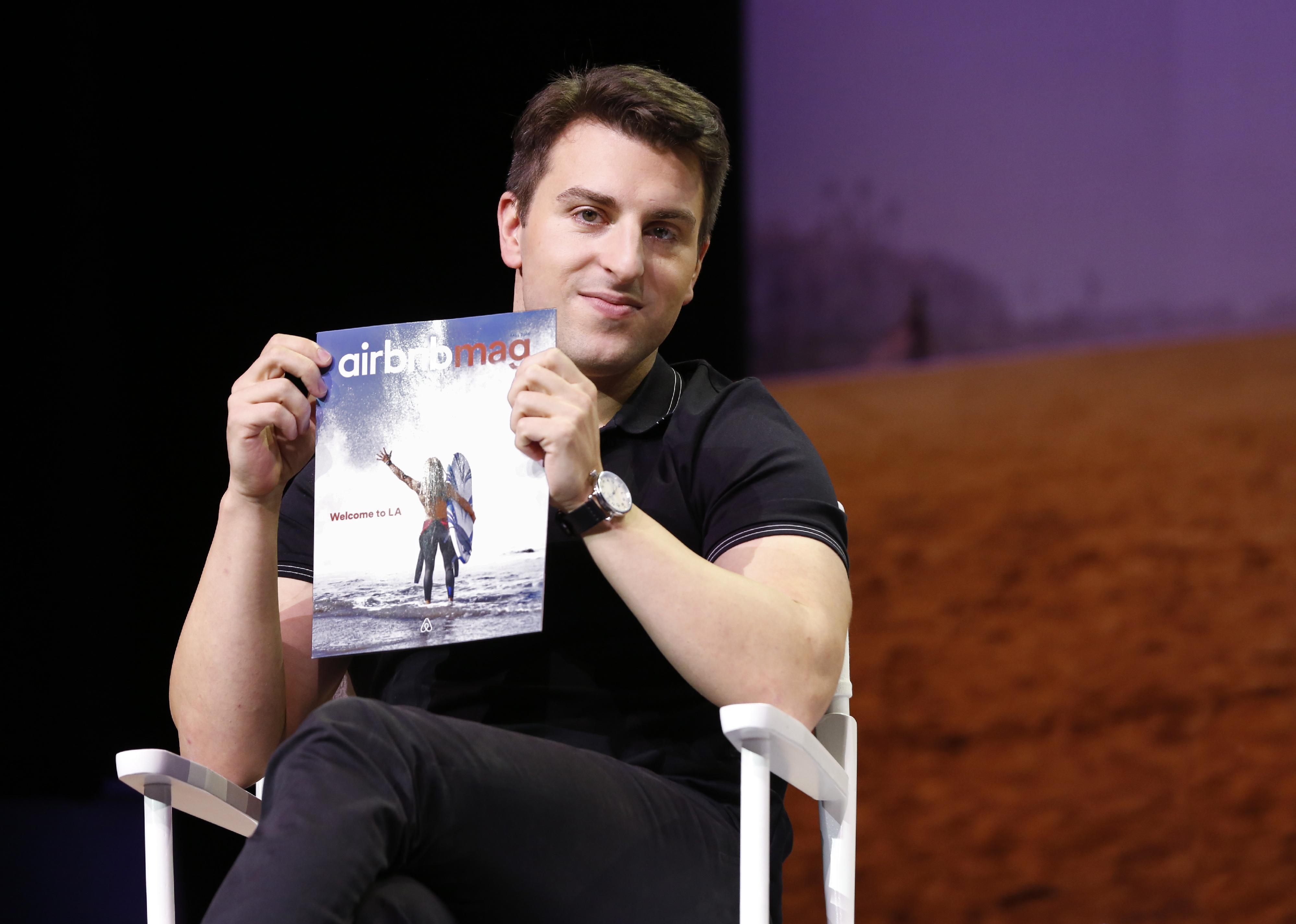 Brian Chesky holding a magazine onstage.