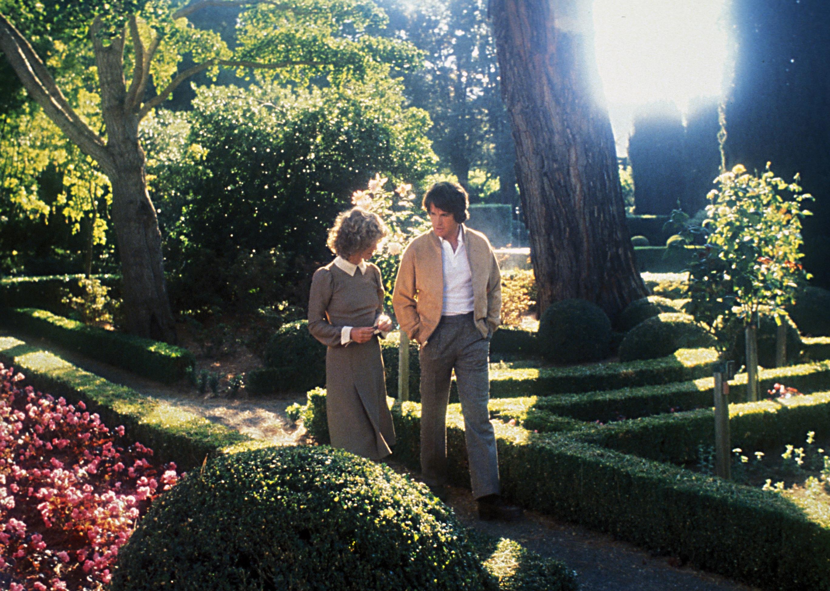 Warren Beatty and Julie Christie walk together in a beautiful garden.