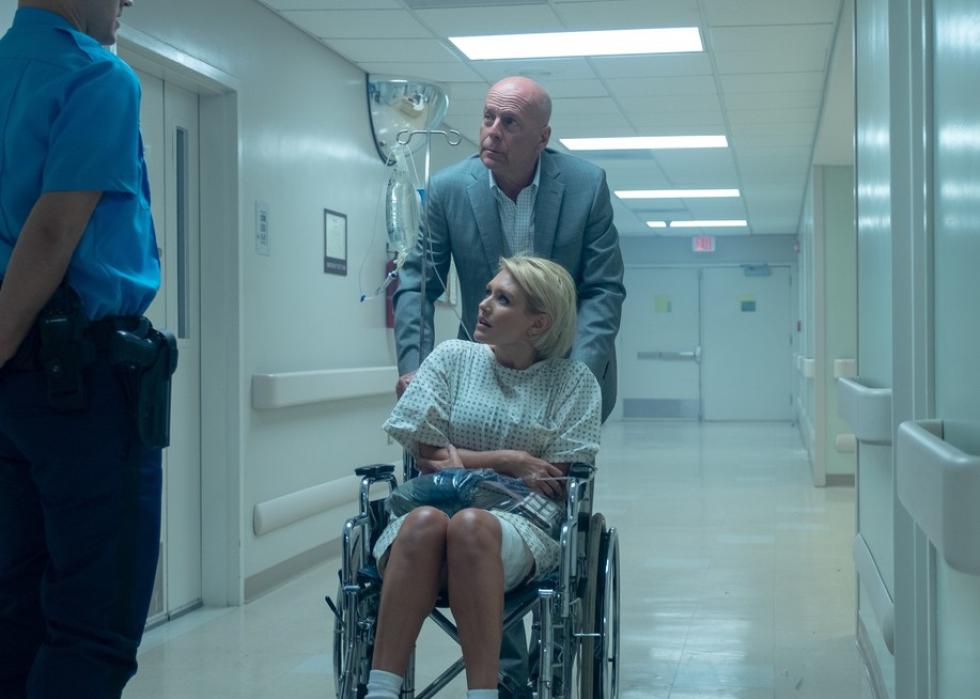 Bruce Willis pushes a woman in a hospital gown and wheelchair down the hall past a police officer.