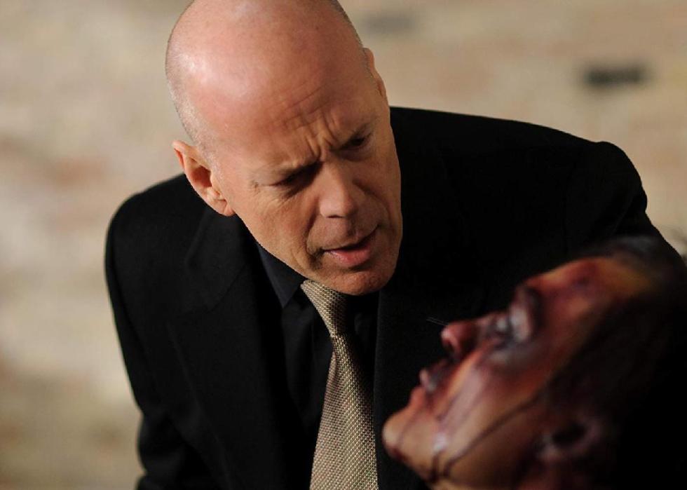 Bruce Willis talks closely to a blurred out man with a beat-up face who looks to be bound.