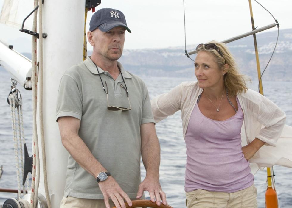 A woman looking at a man while he steers a sailboat.