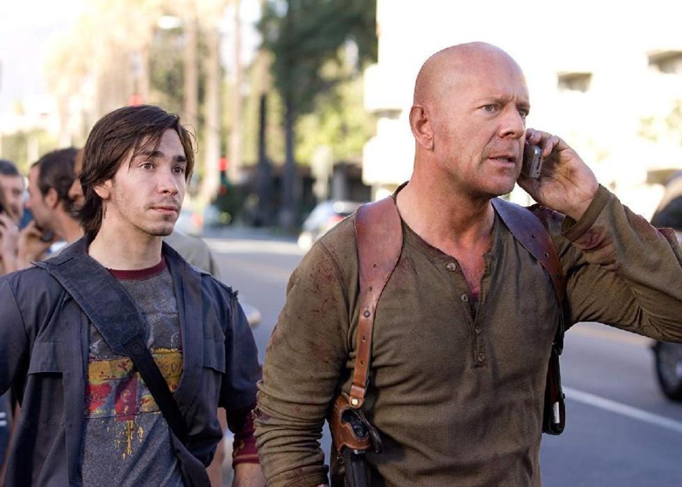 Two men walk together, the older man on the phone with blood on his shirt.