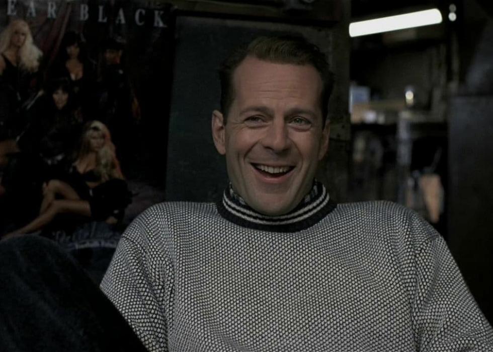 Bruce Willis sits in a chair laughing.