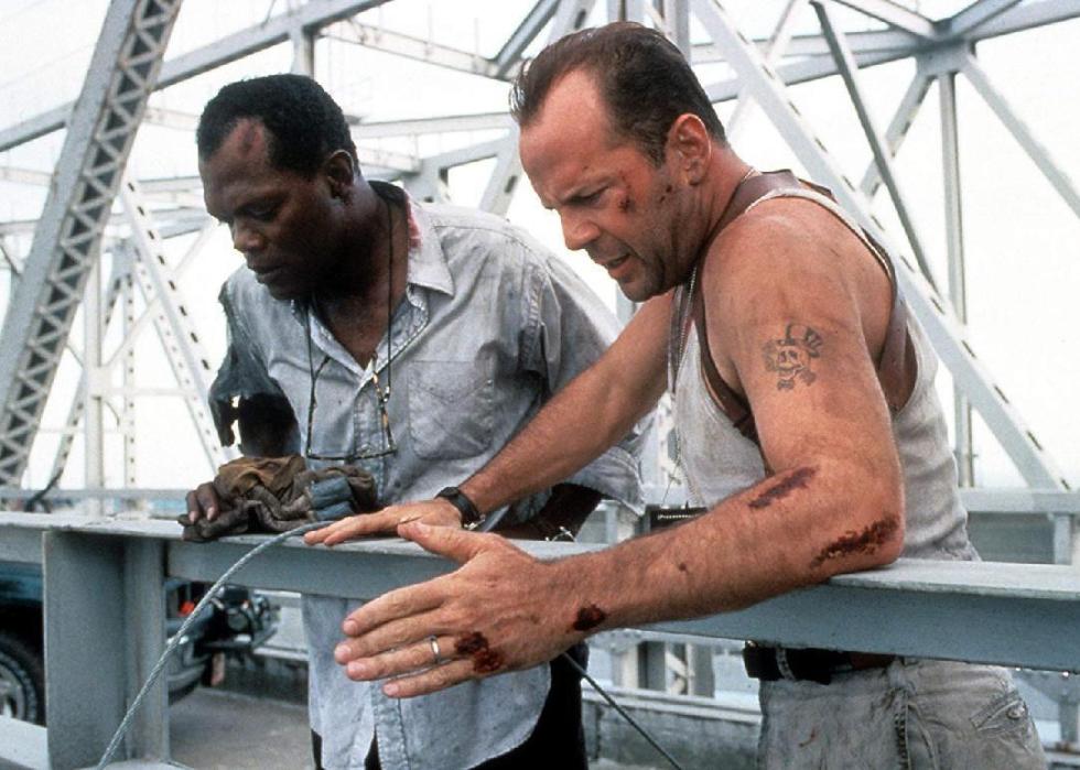 Two beat up men look over the edge of a bridge.