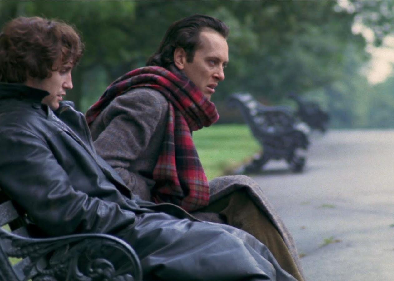 Two men in coats sitting on a park bench together.