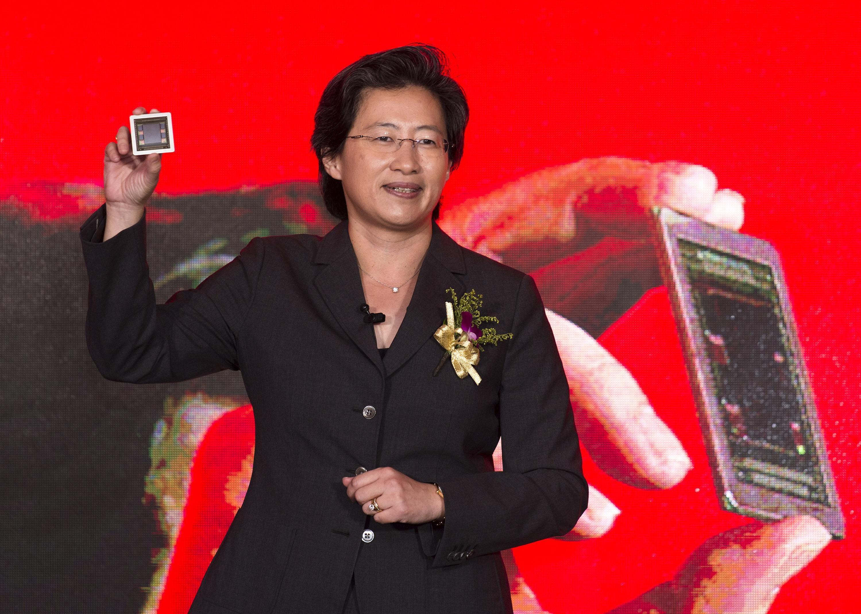 Lisa Su in a black suit holding up a small device.