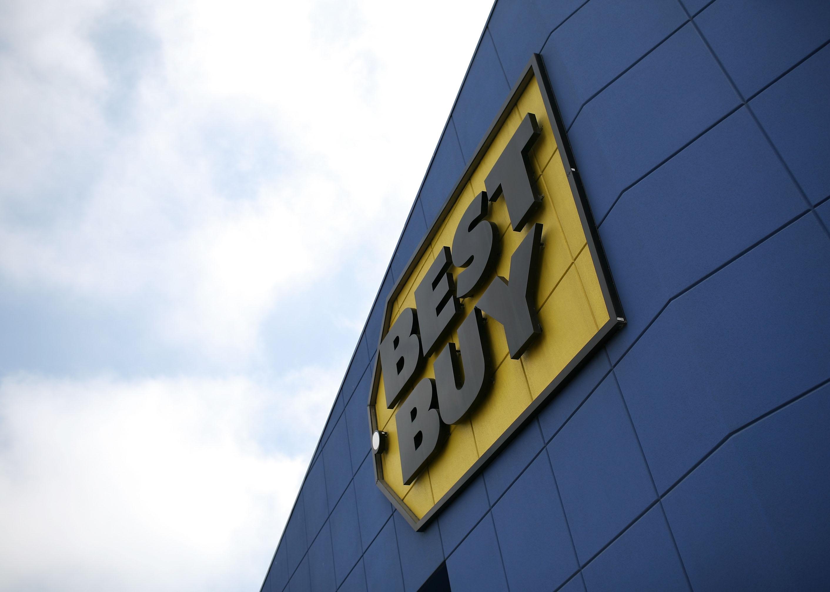 A black and yellow Best Buy sign on a blue building against a blue sky with clouds.