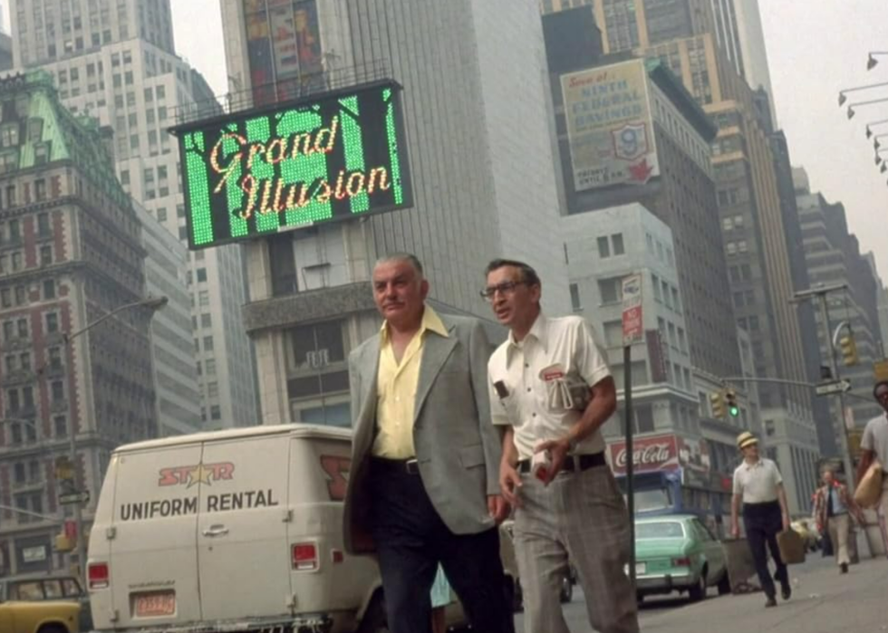 A scene from the film Koyaanisqatsi, with two middle-aged men walking down a busy New York City street. 