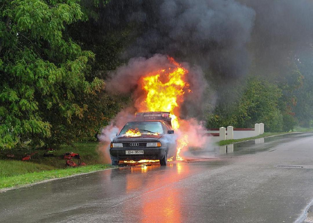 A car on fire on the side of the road. 