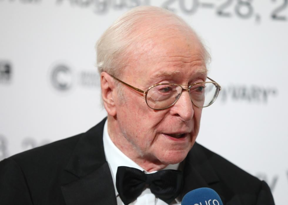 Michael Caine is interviewed at an event wearing a black suit.