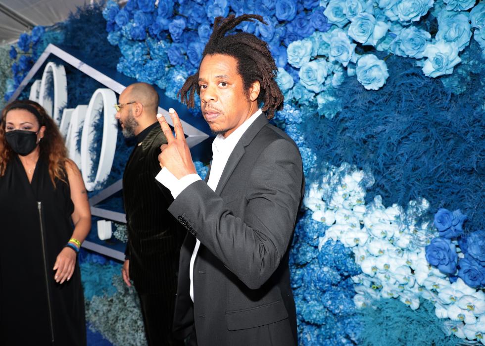 Jay-Z gives the peace sign in front of a wall of blue flowers.