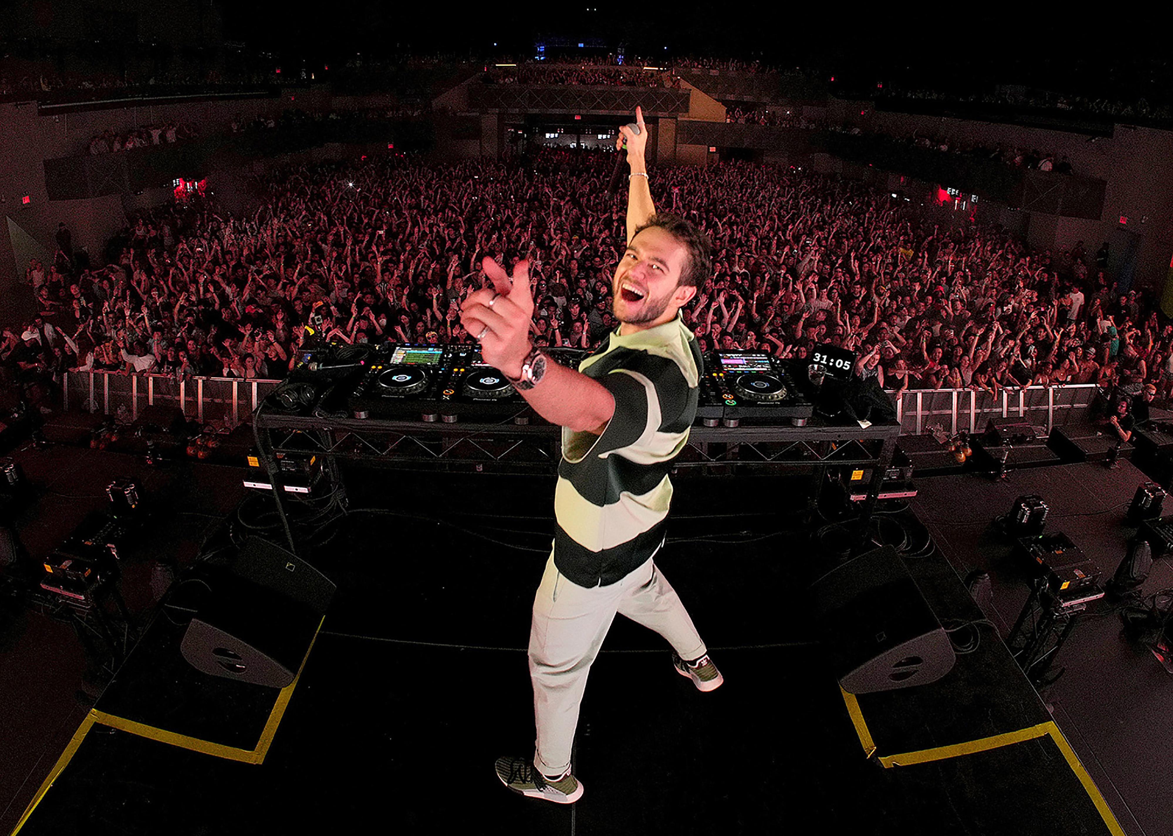 Zedd performing onstage in a black-and-white striped shirt.