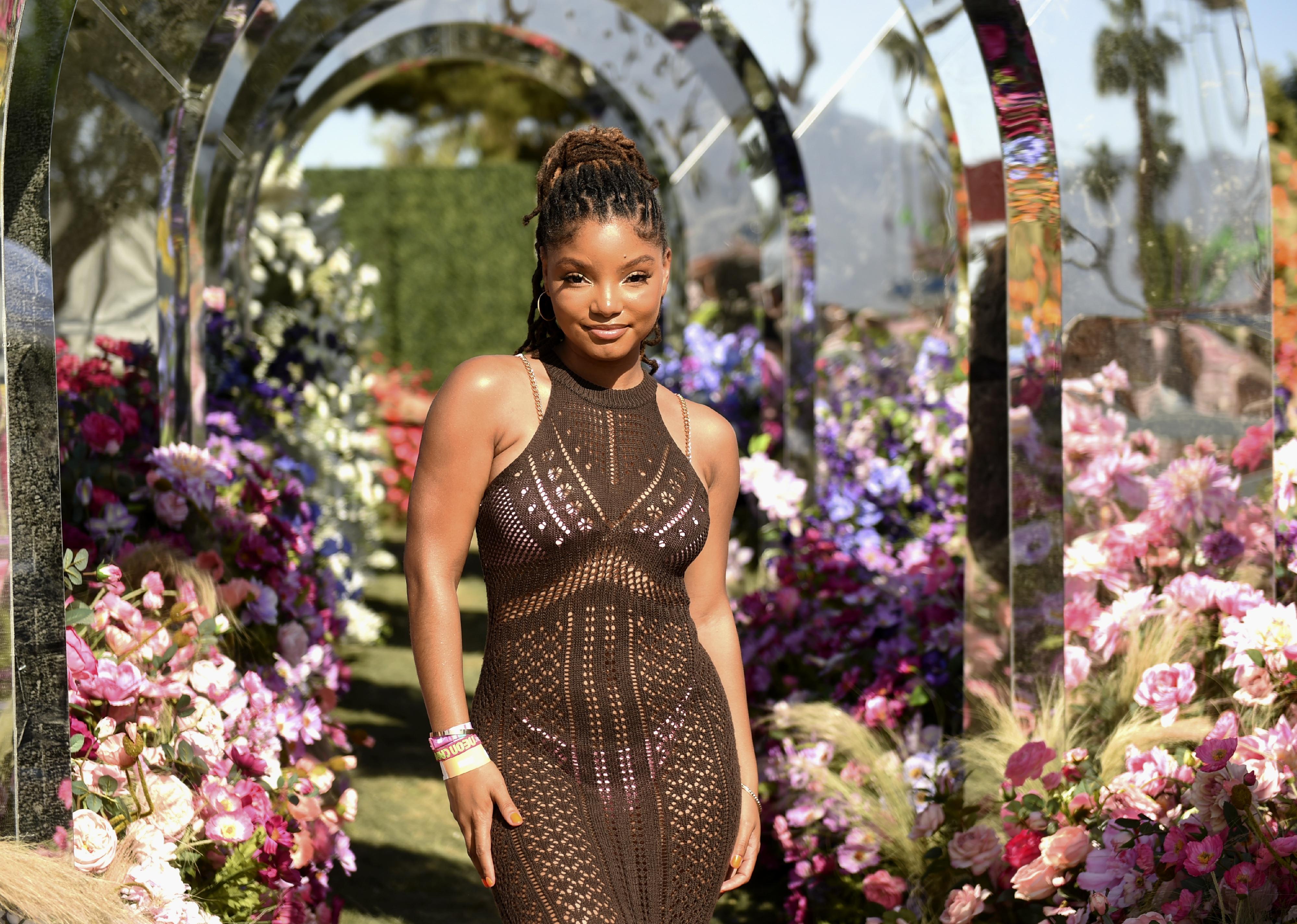 Halle Bailey in a brown knit dress surrounded by flowers.