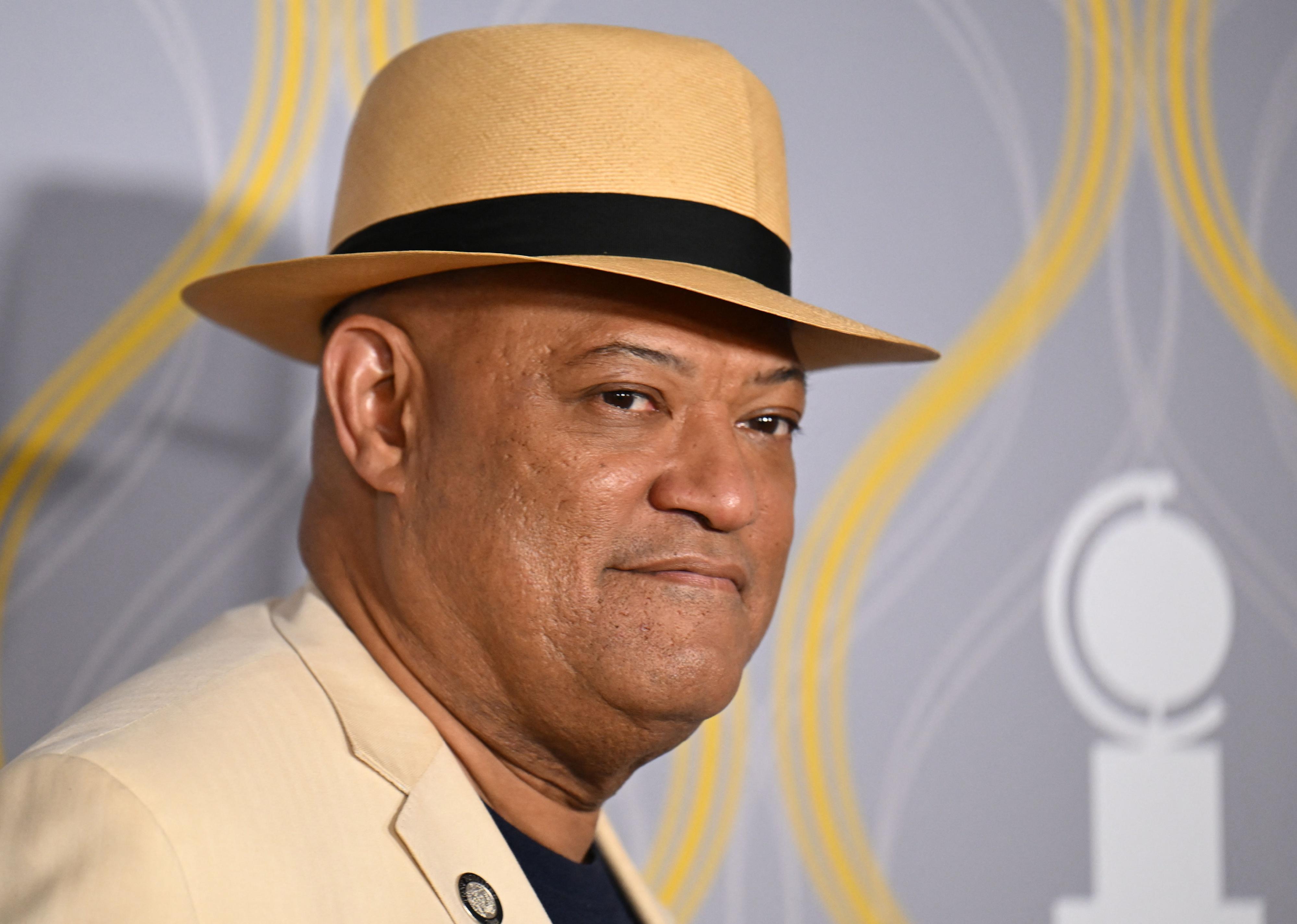 Laurence Fishburne in a tan suit and hat.