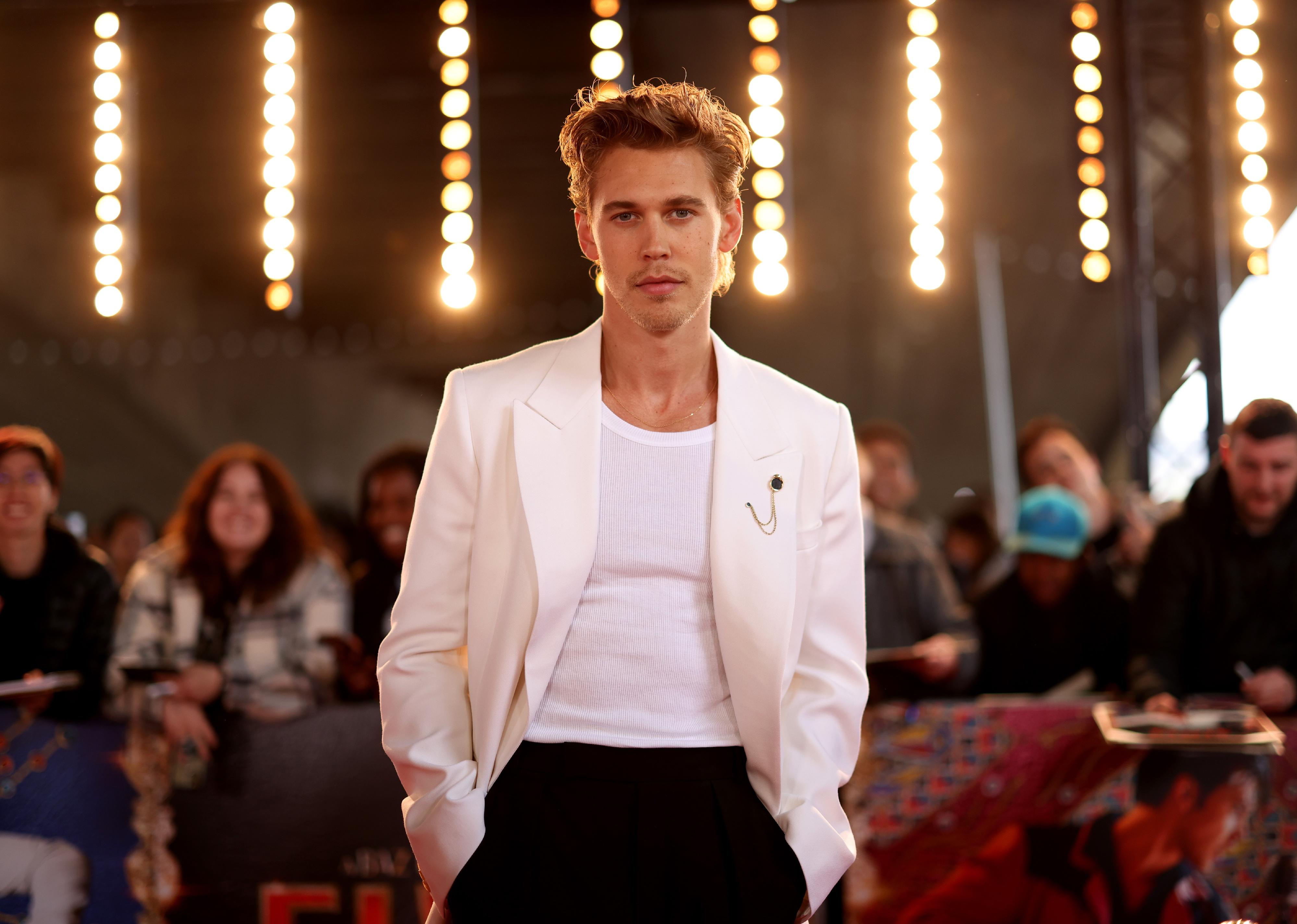 Austin Butler in a white jacket and black pants.