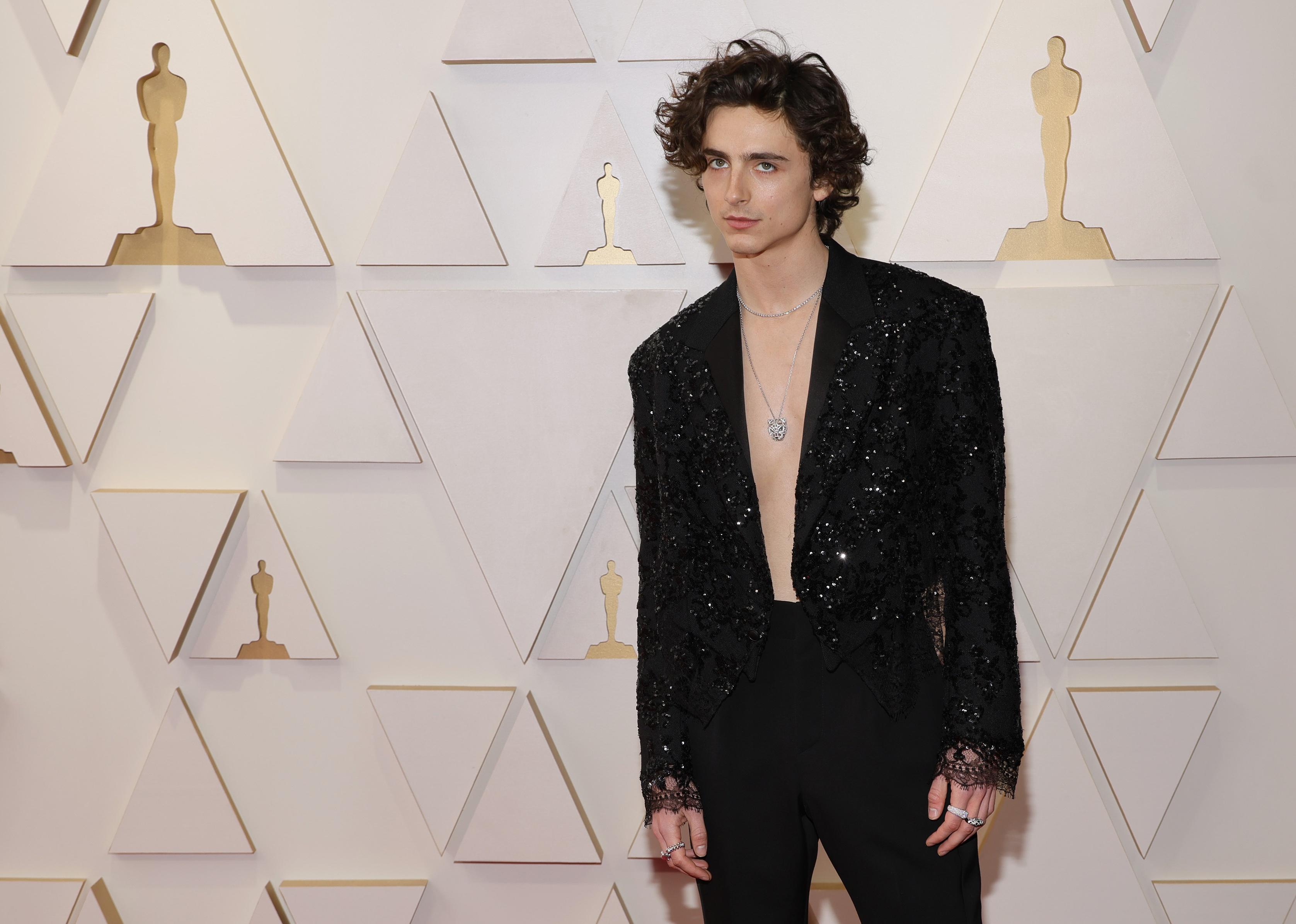 Timothée Chalamet in a black, sparkling open jacket and black pants.