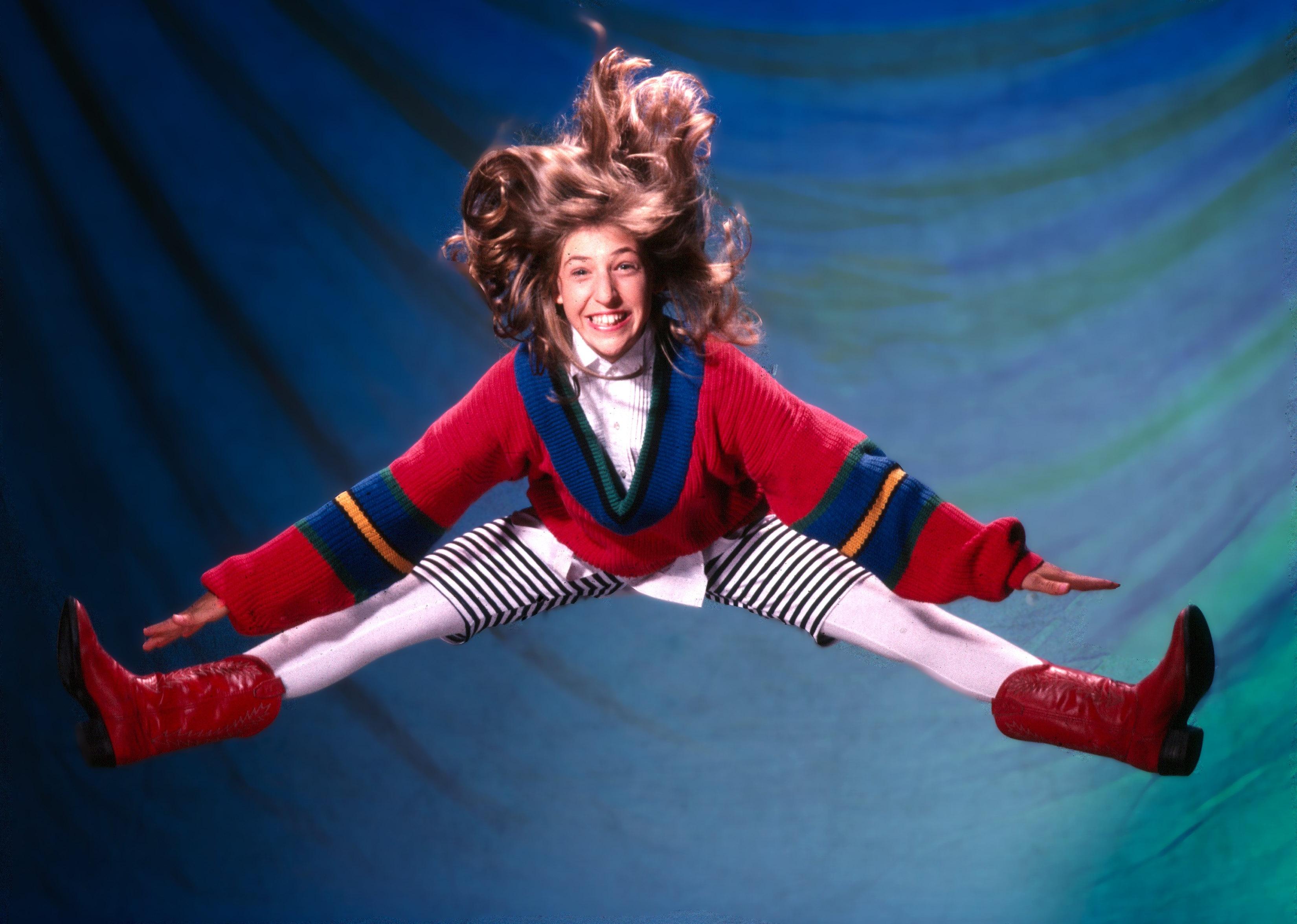 Mayim Bialik jumping in the air and smiling.