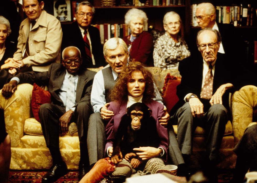 A group of people sit at a couch behind a woman who is holding a monkey.