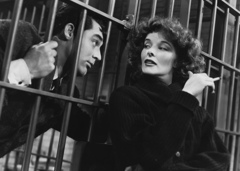 A woman smokes a cigarette while talking to a man behind bars.