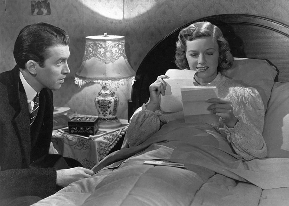 A man sits next to a woman in bed who is reading a letter and smiling.