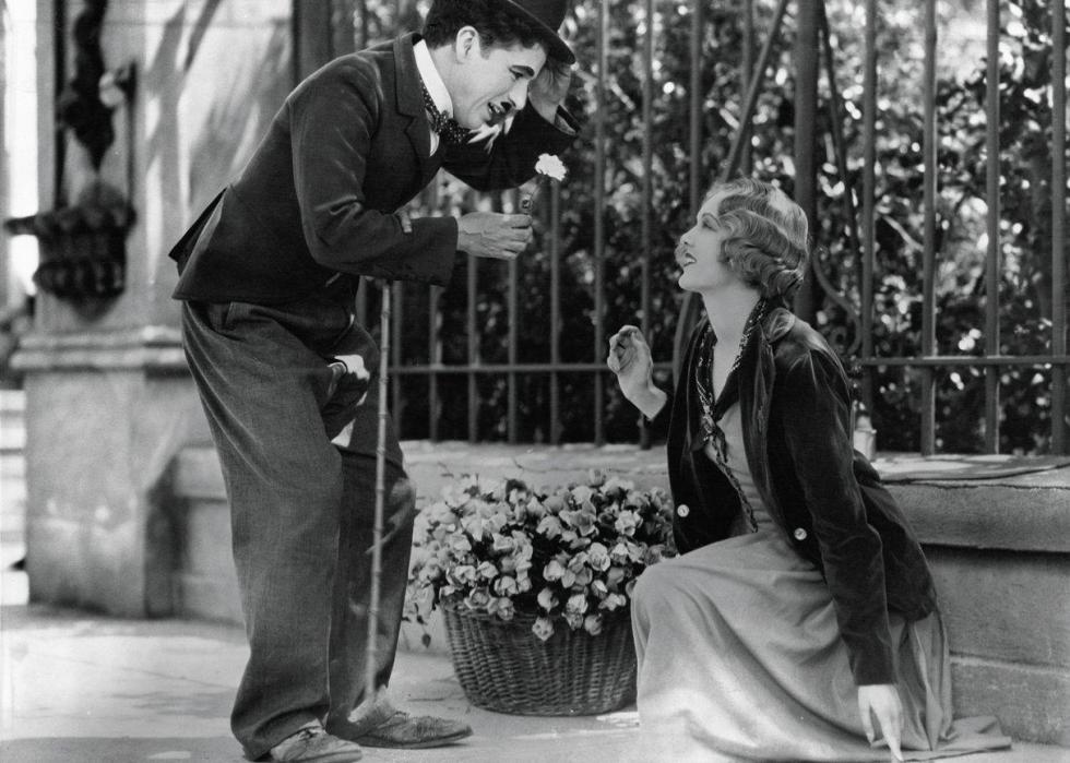 Charlie Chaplin holds a flower for a girl on the sidewalk.