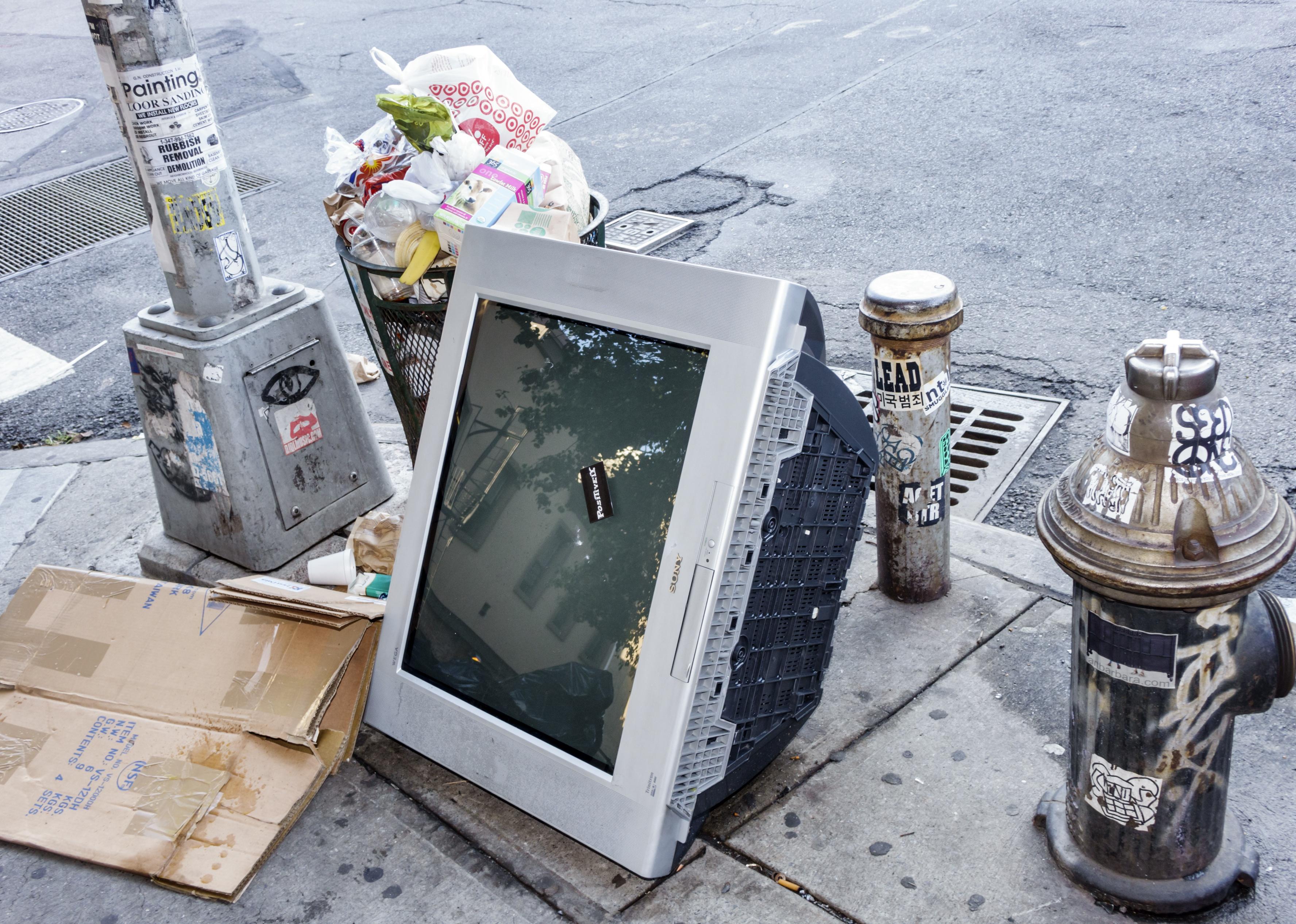 A TV and other garbage dumped on the side of the street.