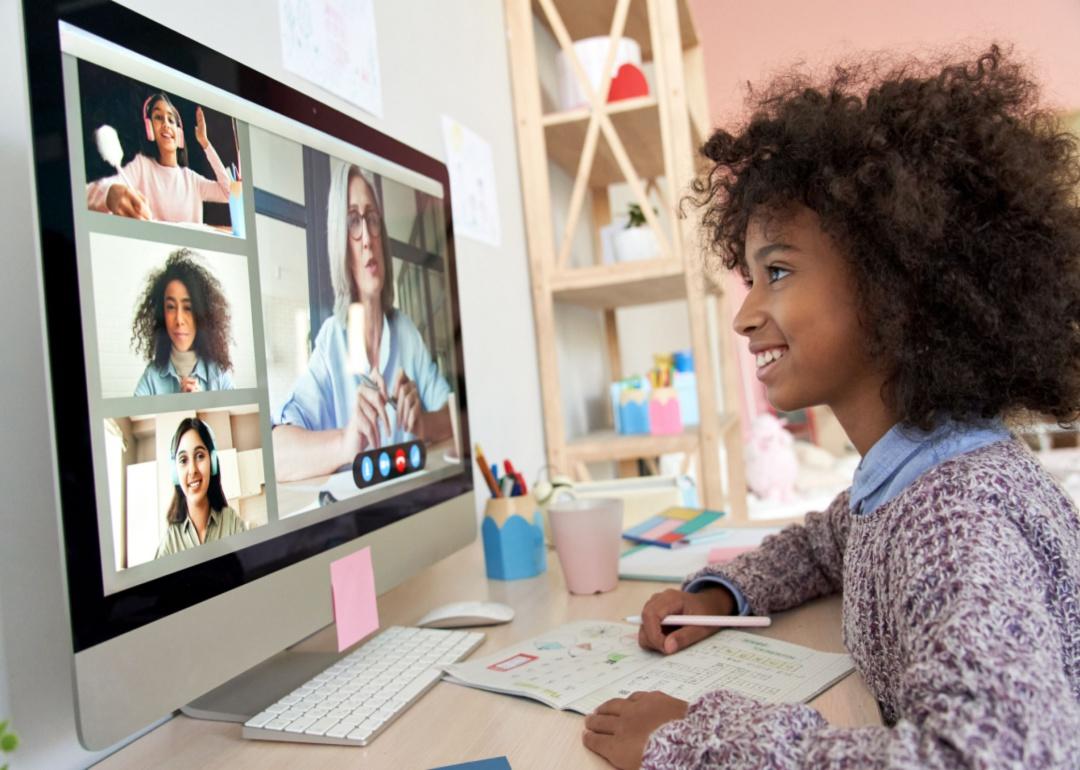 A happy young girl learns remotely with her teacher and classmates.