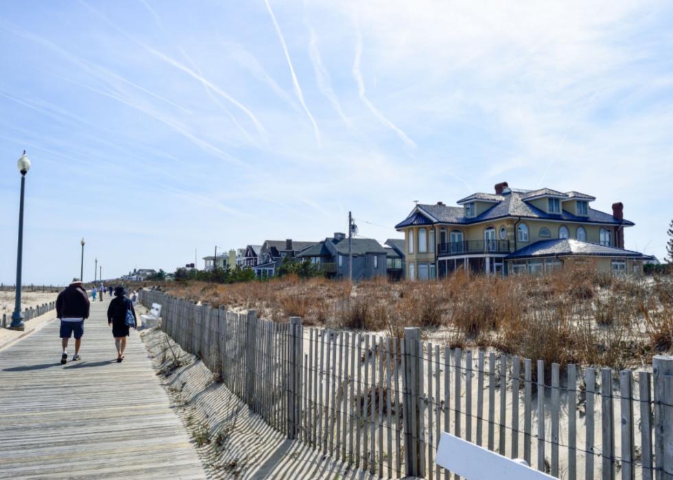 People walking on the boardwalk near large beach homes.