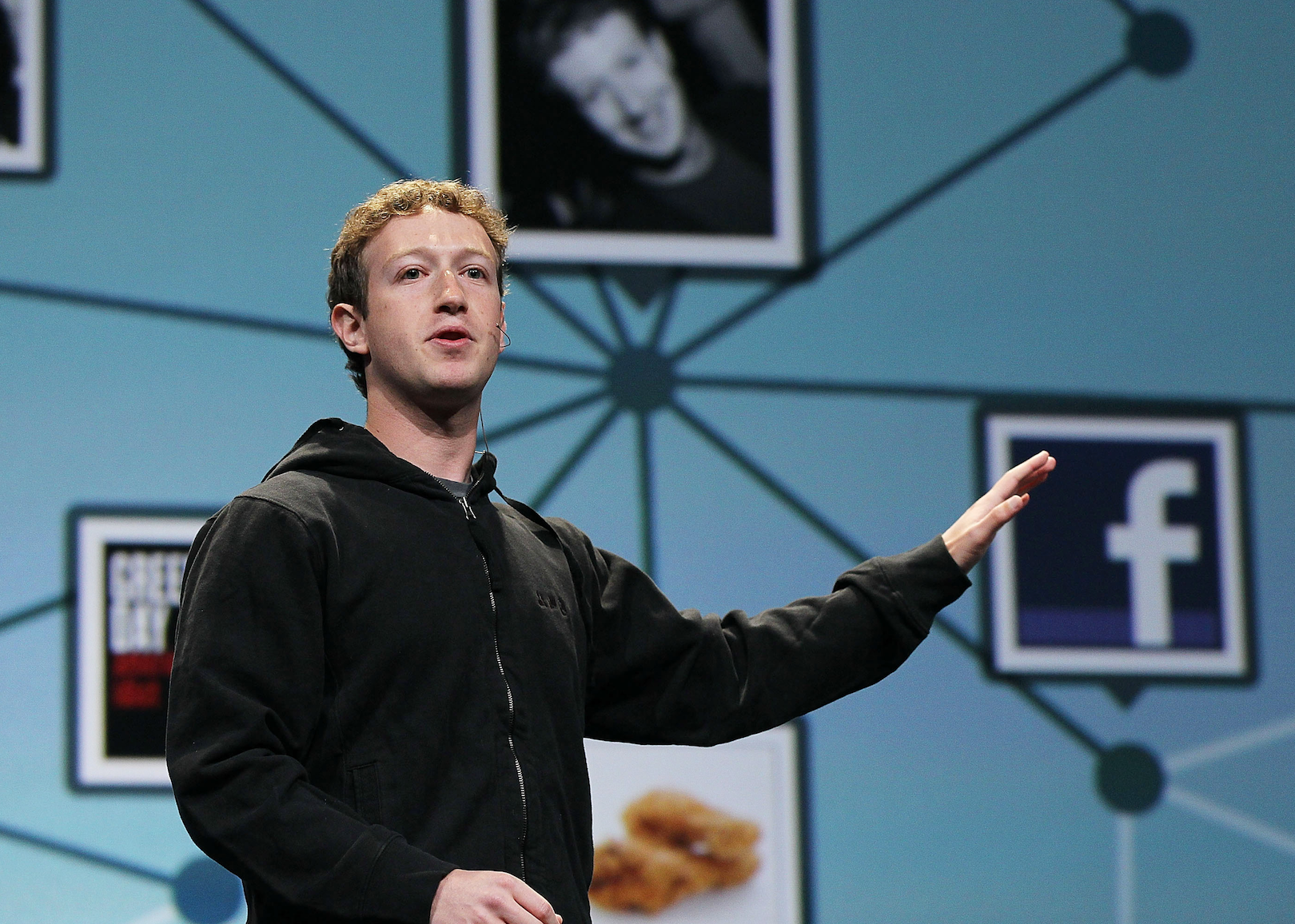 Mark Zuckerberg presenting onstage in front of a Facebook background. 