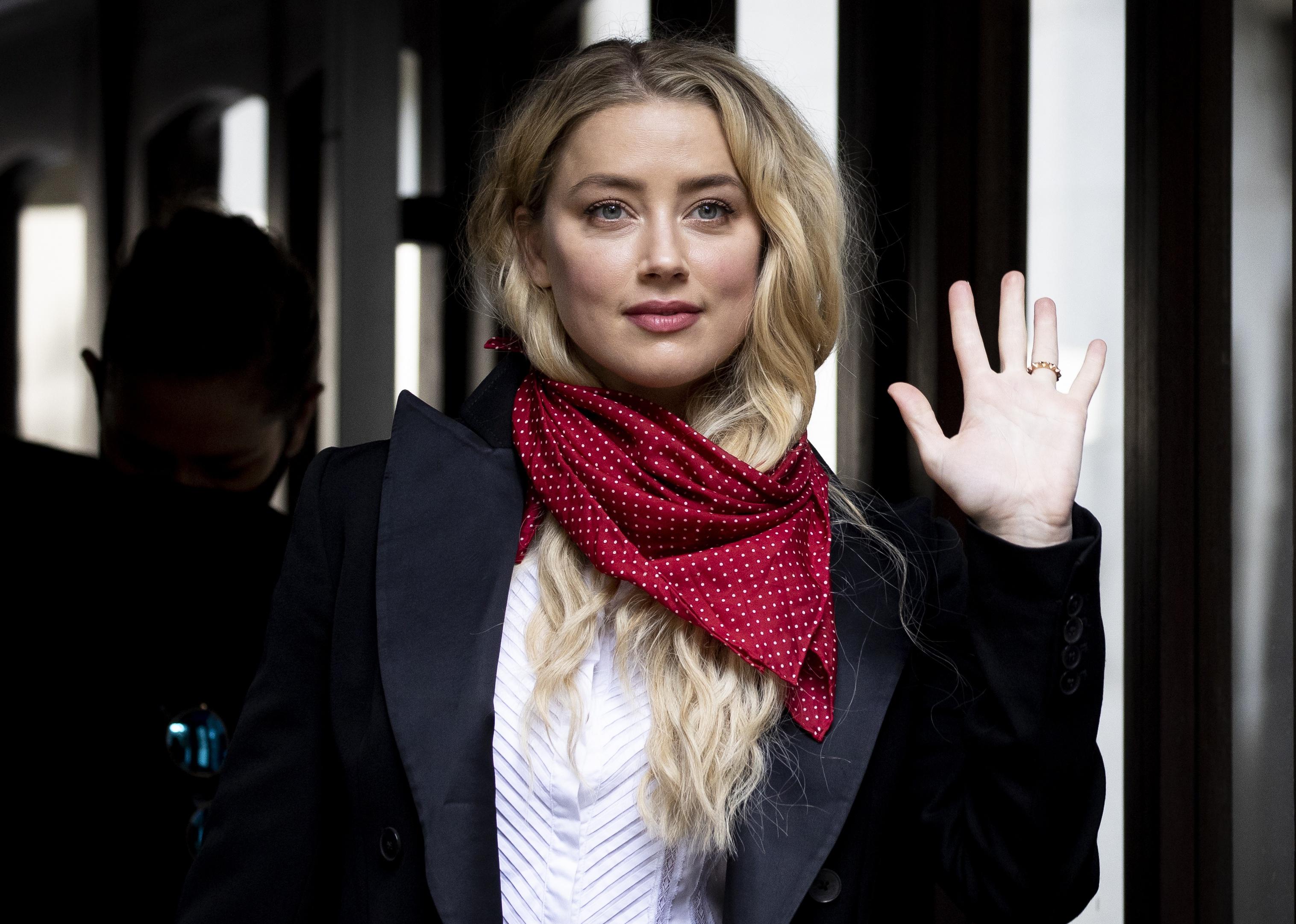 Amber Heard, wearing a red polka dot scarf, waving.