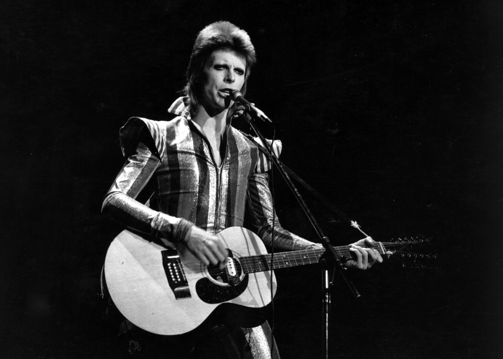David Bowie onstage singing and playing guitar.