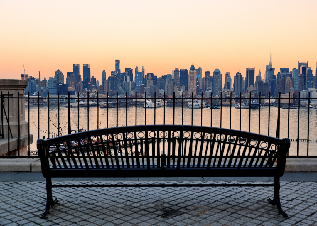 An empty park bench facing New York City across the water.