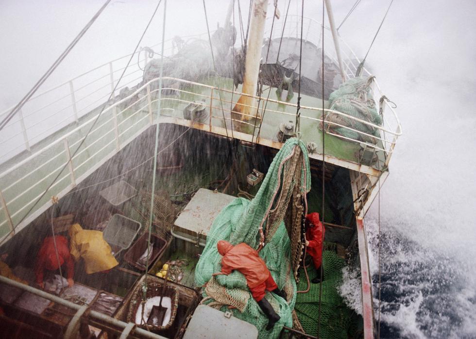 Fishing trawler at sea during storm with crew in raincoats hanging onto everything.
