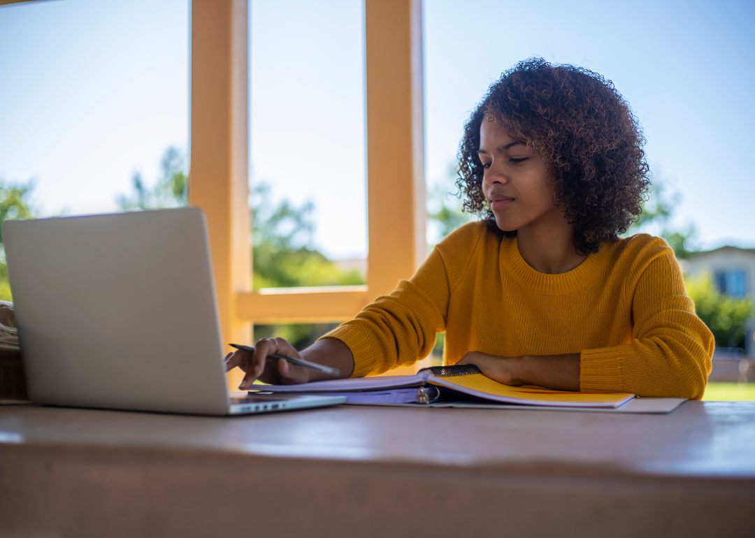 A student in an orange sweater working on a laptop.
