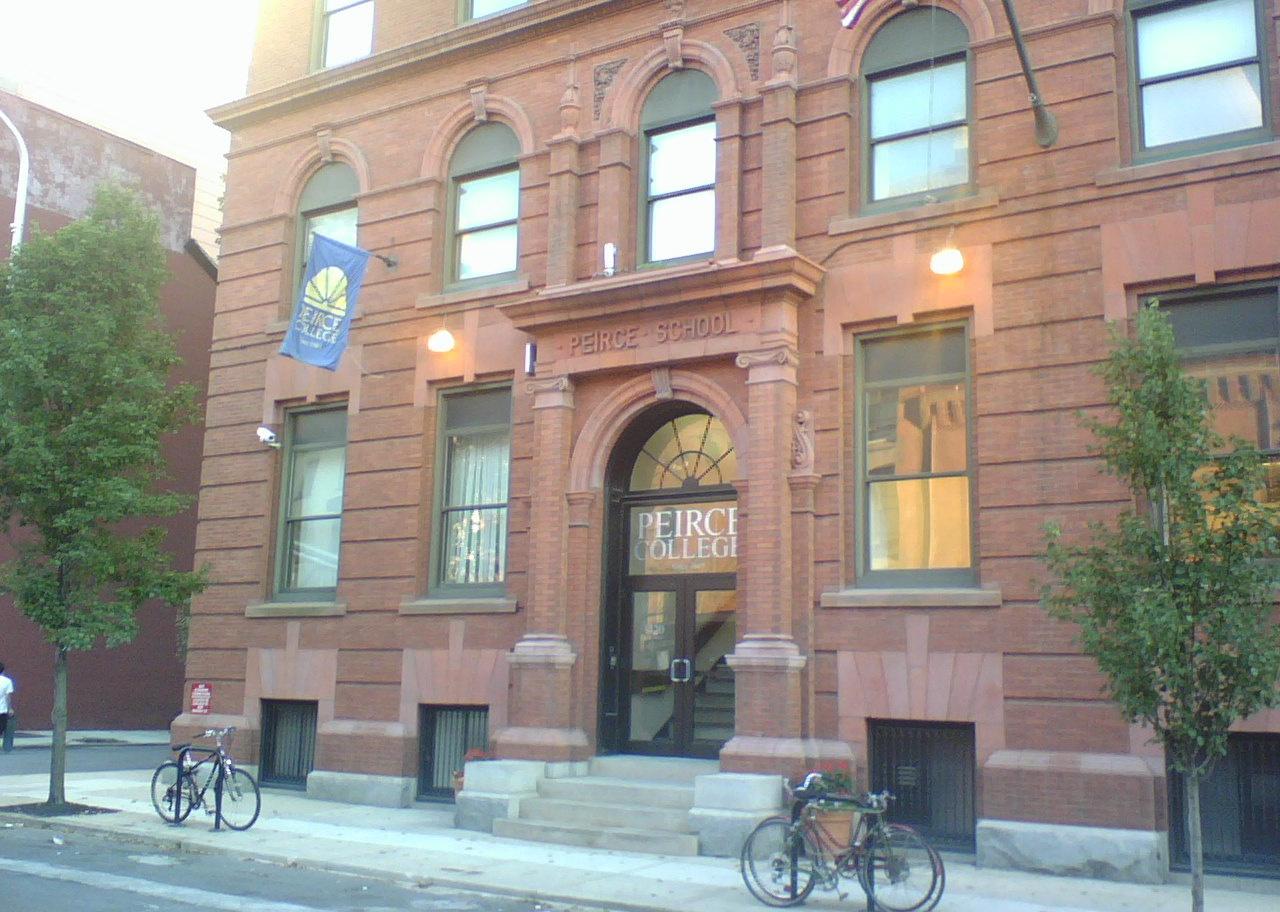 A historic stone building with a Peirce College flag in front.