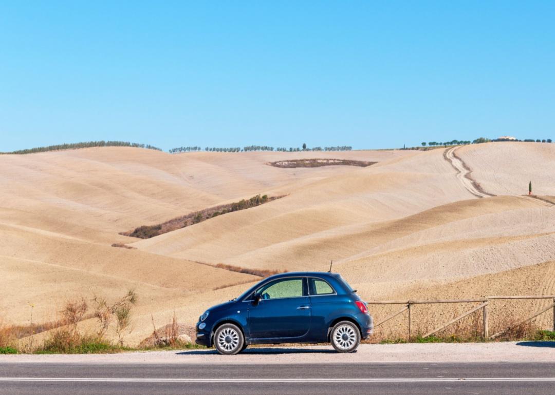 A black Fiat 500 parked in front of a rural field.