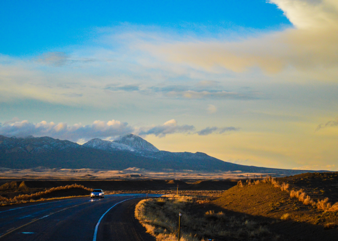 A car driving on a road with mountains in the background in the evening.